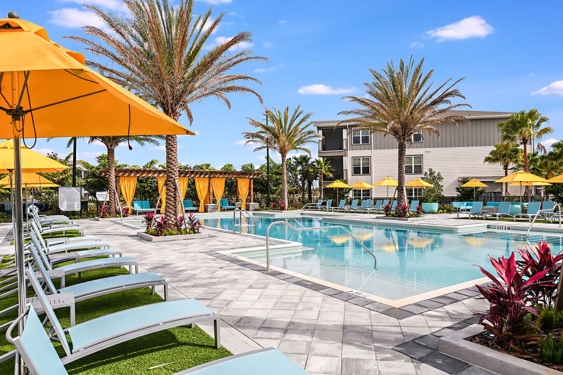 apartment with large swimming pool in winter garden, surrounded by blue lounge chairs with orange umbrellas, and cabanas with orange drapes.