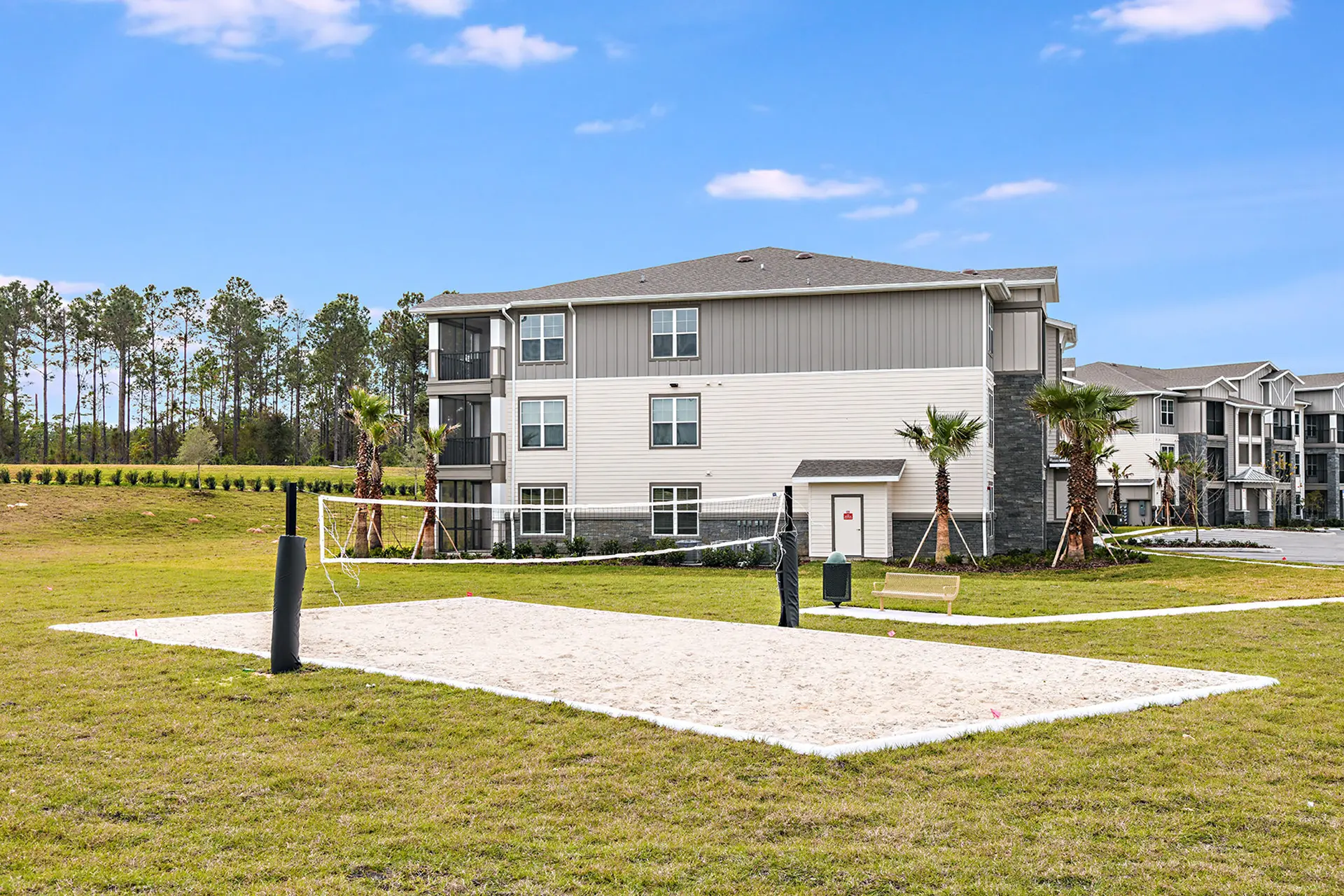 sand volleyball court outside apartments with view of tall pine trees.