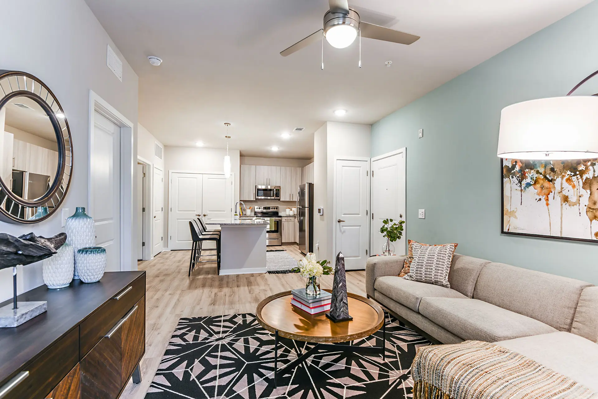 apartment living room with side view of an open kitchen, a seafoam accent wall, gray L shaped couch, and light brown coffee table