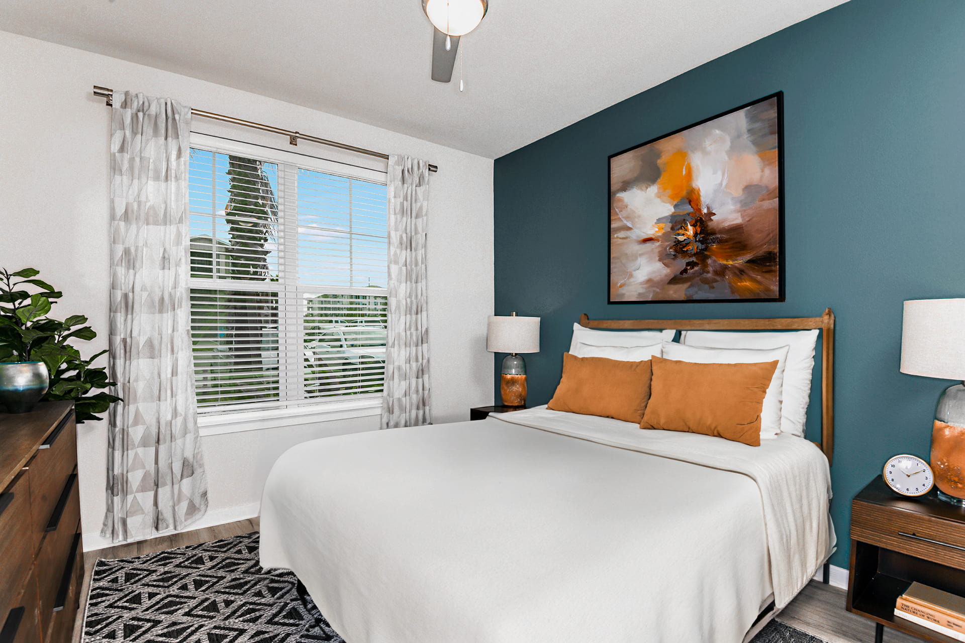 apartment bedroom in winter garden florida with queen sized bed, wood style flooring, a blue accent wall, and large four-pane window.