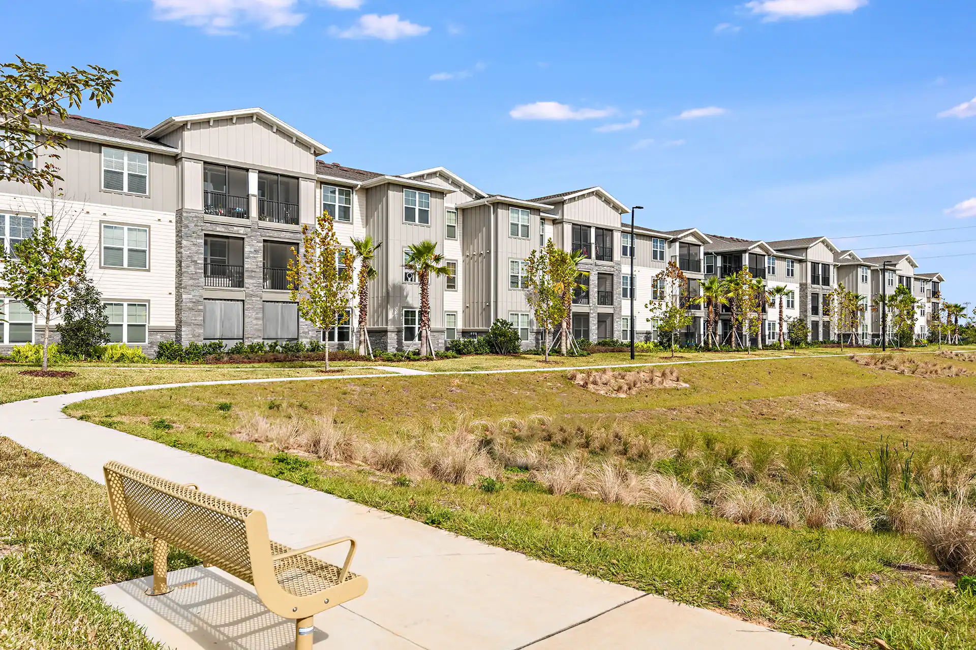 apartment exterior with farmhouse style vertical siding mixed with stone and white brick, and a paved track surrounding a park.