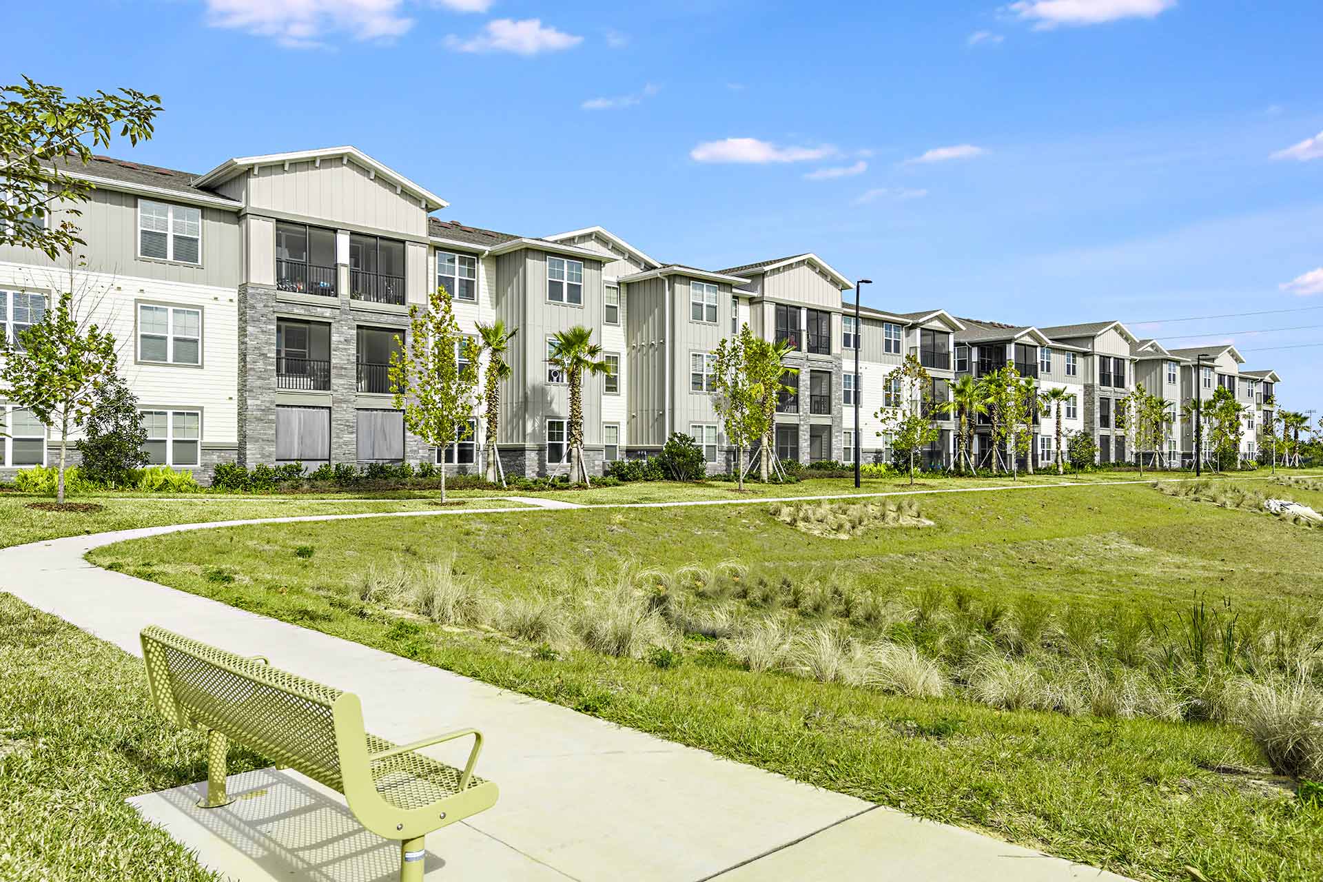 apartment exterior with vertical siding mixed with stone and white brick, and a paved track surrounding a park